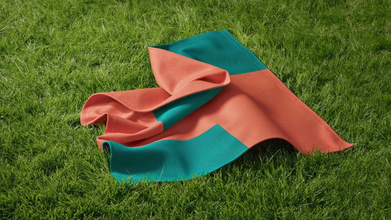 Korálovo-modrozelená piknikový deka částečně rozložená na zelené trávě