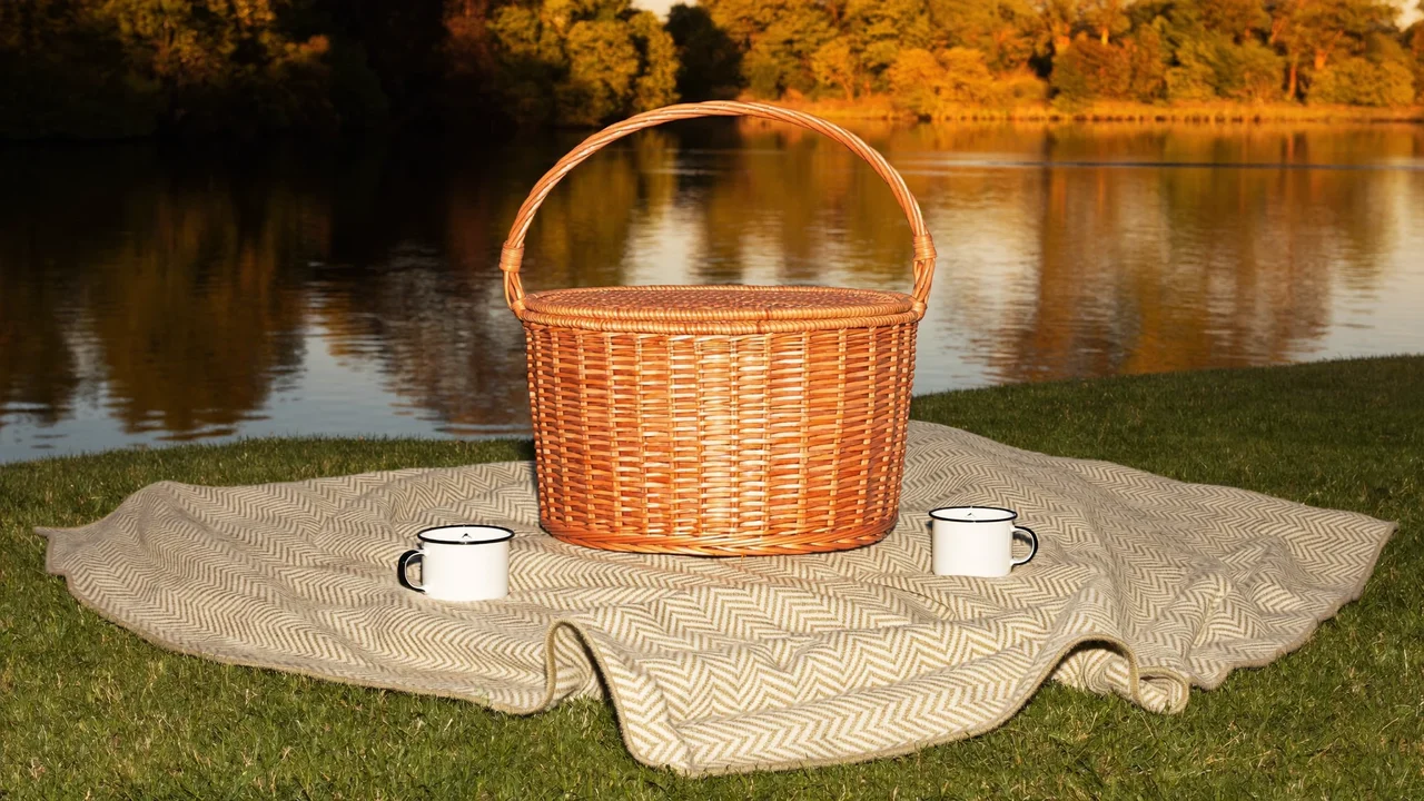 Piknik u klidného jezera při západu slunce s dekou, košem a hrnky